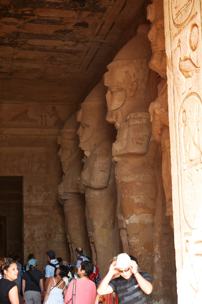 Inside the Great Temple's first hall, where eight pillars fronted by standing Osiride statues of Ramesses II carry the ceiling — all of it carved from solid rock rather than built up in blocks.