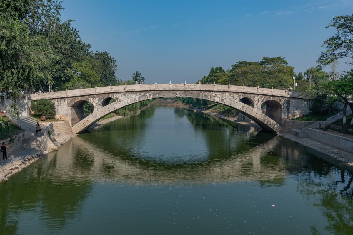 A full elevation of the bridge across the water, its flattened 37-metre span rising in a single low arc with two open spandrel arches at each end.