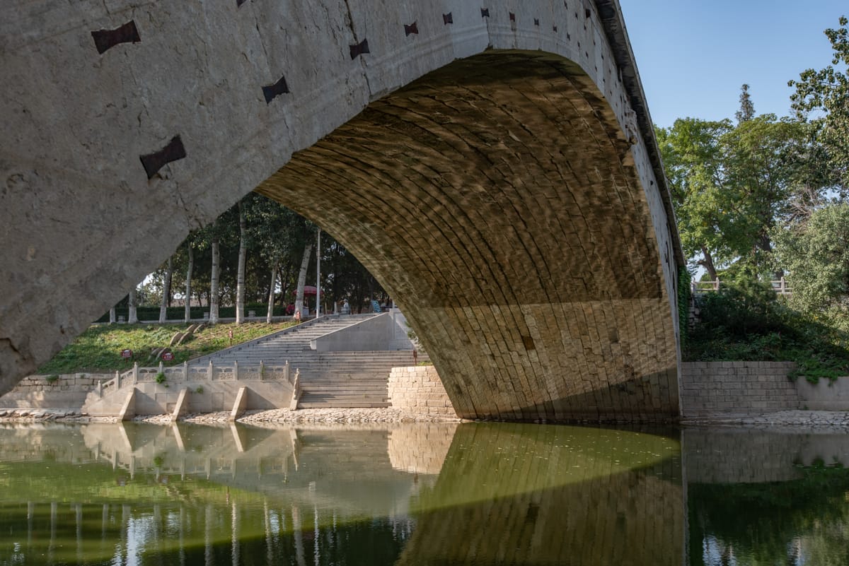 The underside of the main arch, revealing the curved limestone voussoirs of the barrel and the dark iron 'butterfly' cramps that tie the arch stones together.
