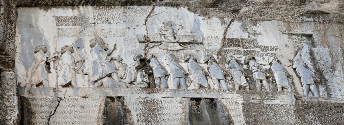 The full relief panel, about 3 m high and 5.5 m wide. Darius stands at the left with two attendants; Gaumata lies under his foot; nine roped rebel kings face him, and the winged figure floats above the line.