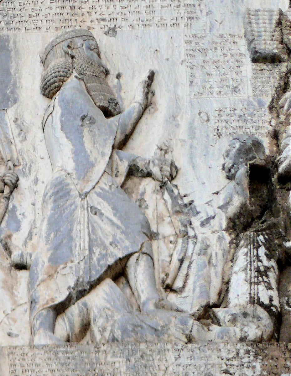 Darius, carved life-size at 1.72 m, with his left foot on the chest of Gaumata. His beard is a separate block of stone, pinned into the cliff with iron and lead.