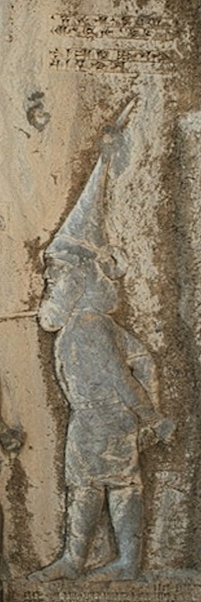 Skunkha the Saka, the last figure in the line. Cutting him in meant chiselling away a strip of the already-finished Elamite text — which then had to be copied out again somewhere else on the cliff.