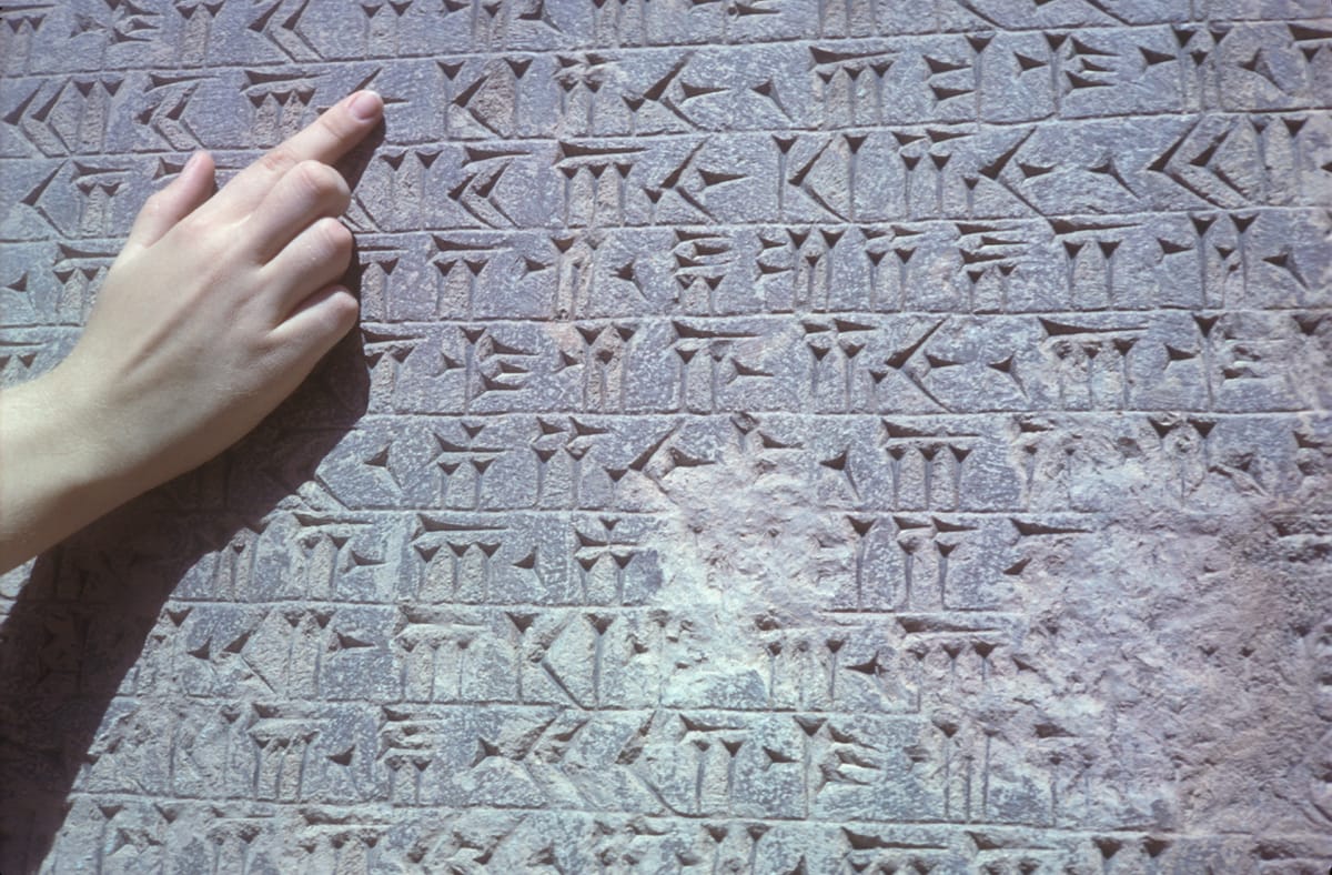 Cuneiform on the cliff at close range. The pitted patch at centre-right is damage; the monument has been chipped by weather, dissolved and re-crusted by rainwater, and reportedly used for target practice by soldiers during the Second World War.