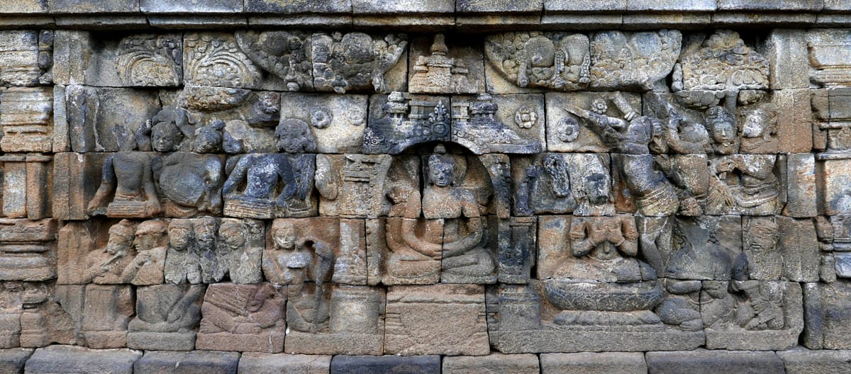 One of the roughly 2,672 carved relief panels lining the galleries, depicting a Buddha figure serenaded by an orchestra.