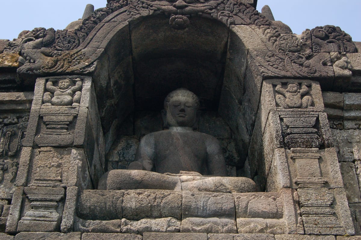 A Buddha statue seated inside one of the perforated, bell-shaped stupas on the monument's circular upper terraces.