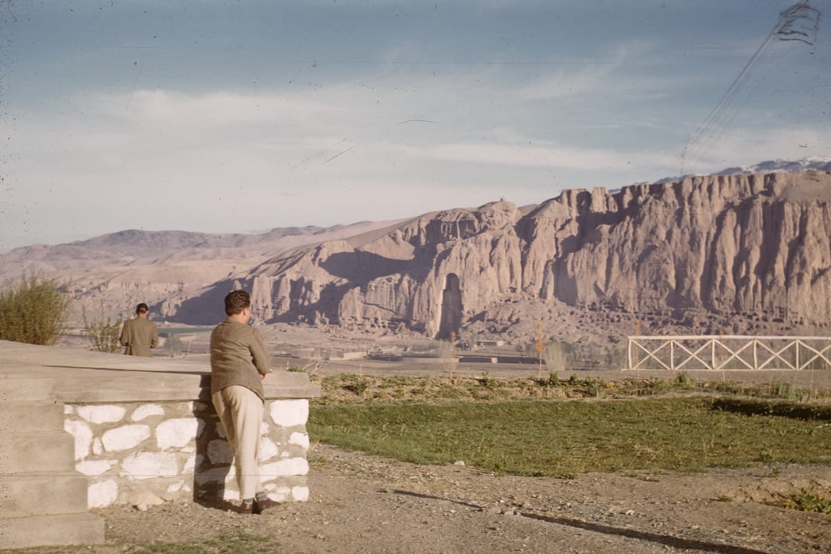 The Bamyan valley in May 1961, with the Western Buddha standing in its niche in the cliff face and the honeycomb of monastic caves around it.