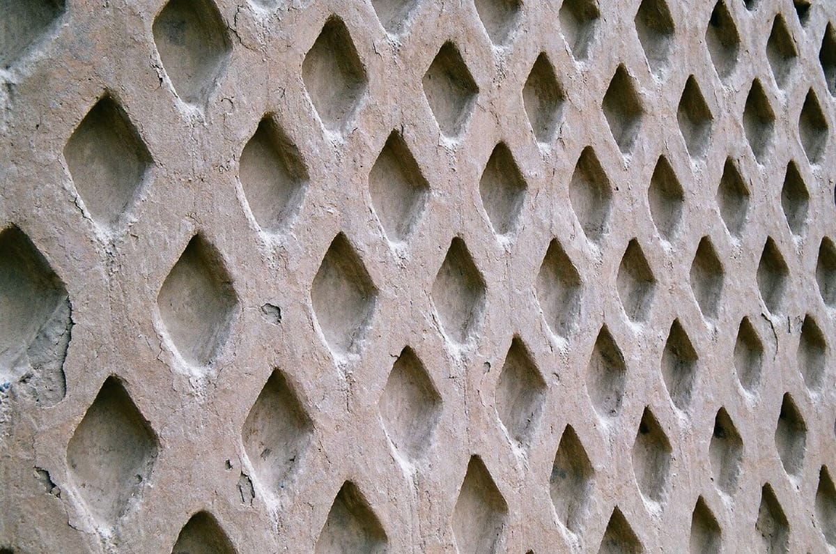 An adobe wall carved in a repeating diamond lattice, widely read as a stylized fishing net — one of the recurring marine motifs of Chan Chan's reliefs.