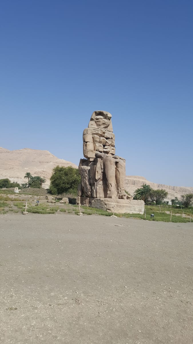 Looking up at one of the colossi, giving a sense of the roughly 18-metre height of statue plus base. Each figure was carved, as far as can be told, from a single enormous block of quartzite sandstone.
