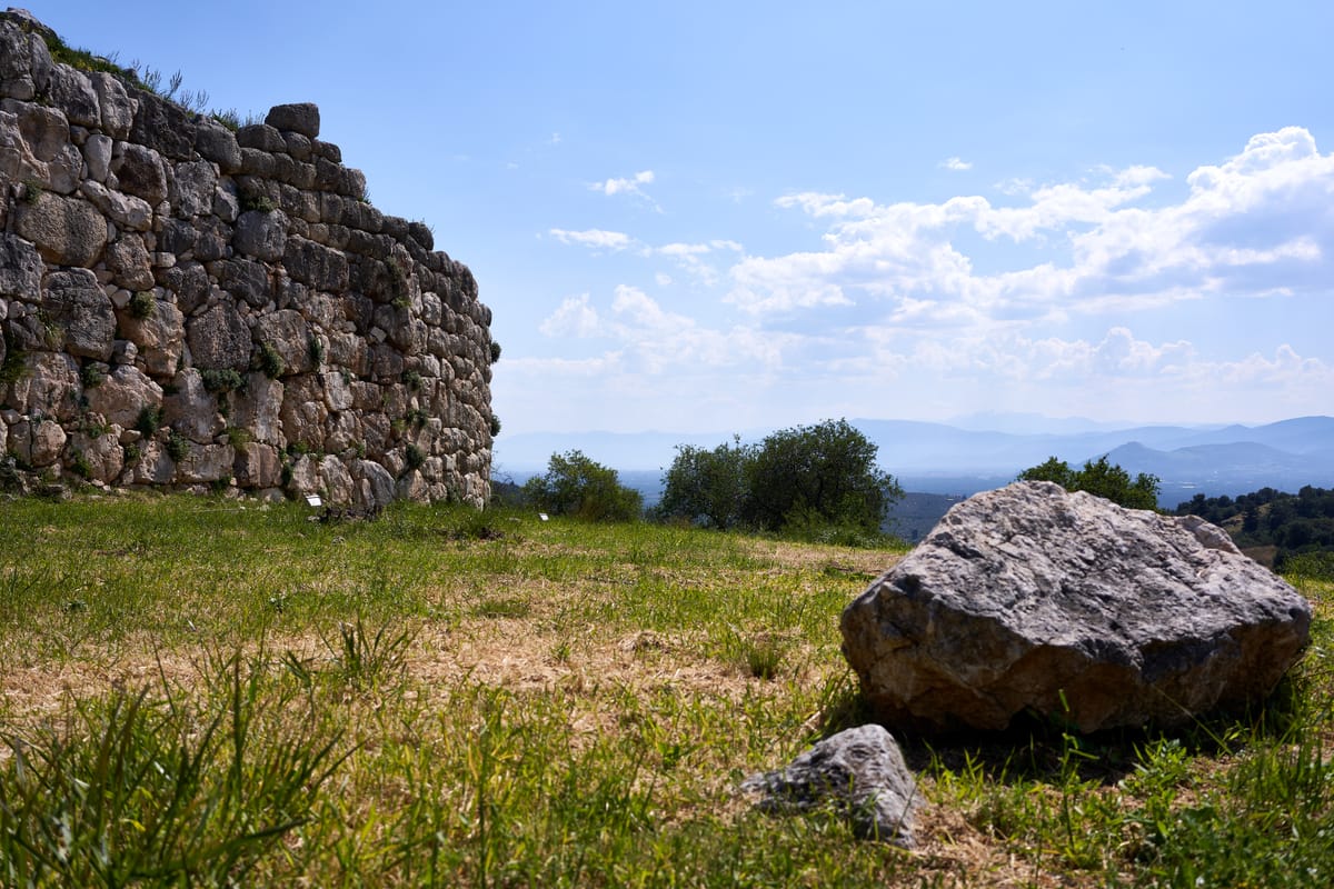 A stretch of Mycenae's Cyclopean fortification wall, built from massive, roughly-fitted limestone boulders with smaller stones packed into the gaps.