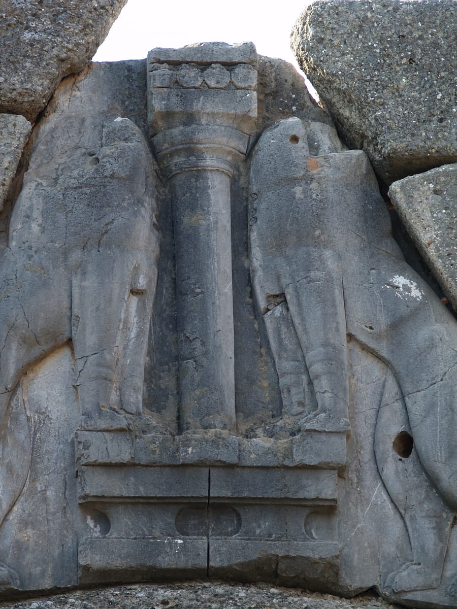 Close view of the relieving triangle above the Lion Gate's lintel, carved with two confronted lionesses flanking a Minoan-style column.