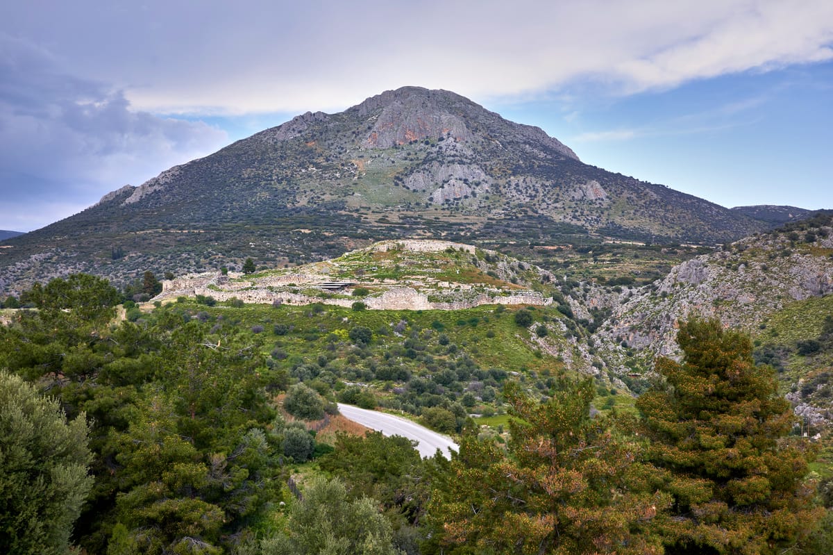 The citadel of Mycenae seen from the direction of the Treasury of Atreus, showing the hilltop fortress and its Cyclopean circuit wall in context.