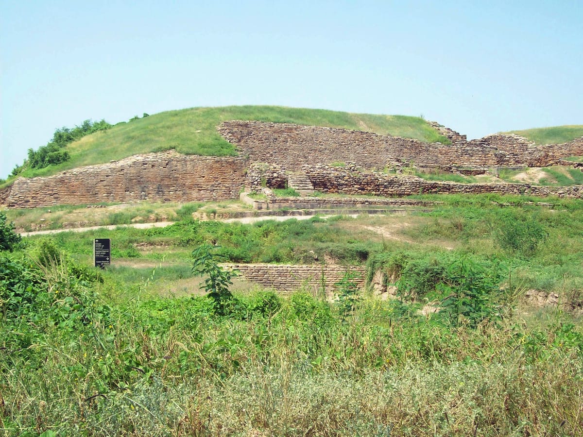 The massive stone rampart of Dholavira's fortified citadel, with a modern signpost pointing toward the citadel and the site's reservoirs.