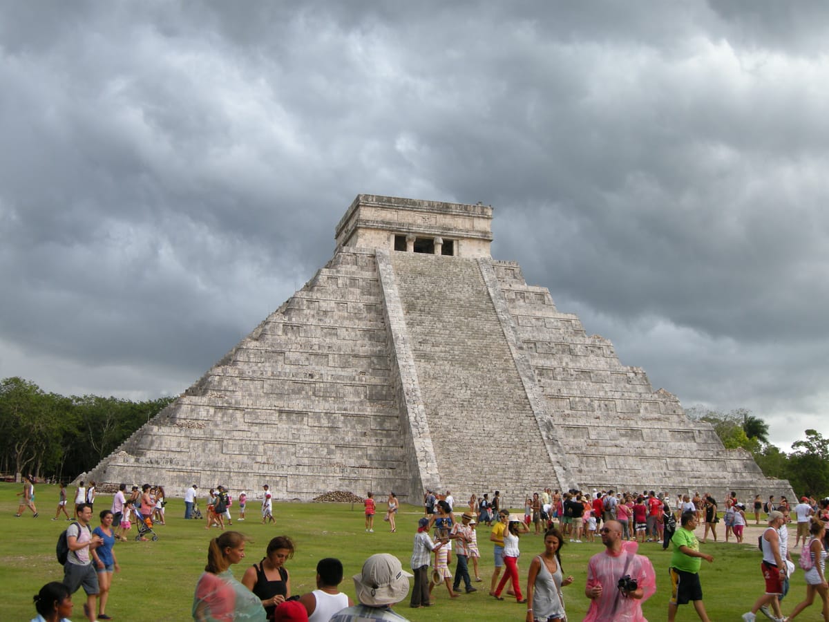 A corner view of El Castillo showing the pyramid's nine stacked terraces and the steep balustraded stairways climbing each face.