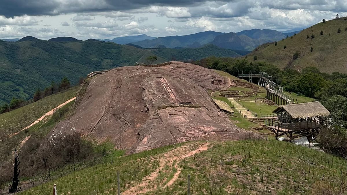 The whole carved outcrop rising above the wooded Andean foothills around Samaipata, showing the scale of the single sculpted hill above the valley.