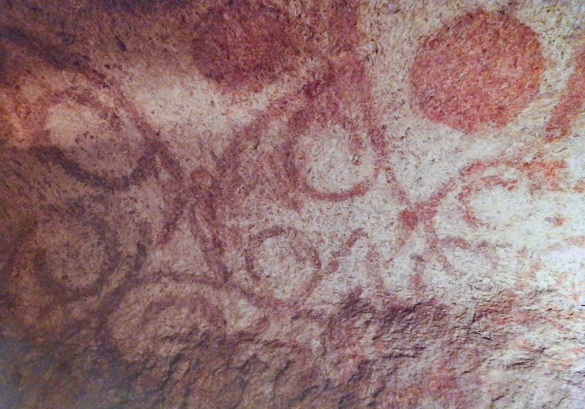Red-ochre spiral and disc motifs painted directly onto the carved limestone ceiling of the Oracle Chamber.