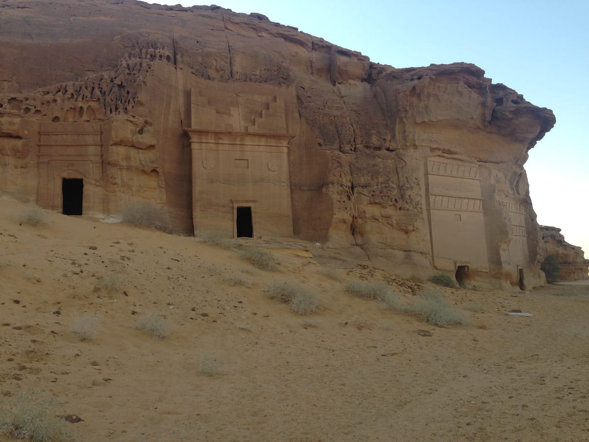 A row of monumental tombs cut side by side into a single sandstone massif, their facades topped with the stepped merlon crowns characteristic of Nabataean funerary architecture.
