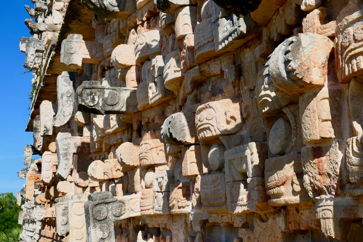 Close view of the mask ranks: goggle eyes, fanged mouths, brow plates and curled snouts, every element a separate carved block set into the wall.