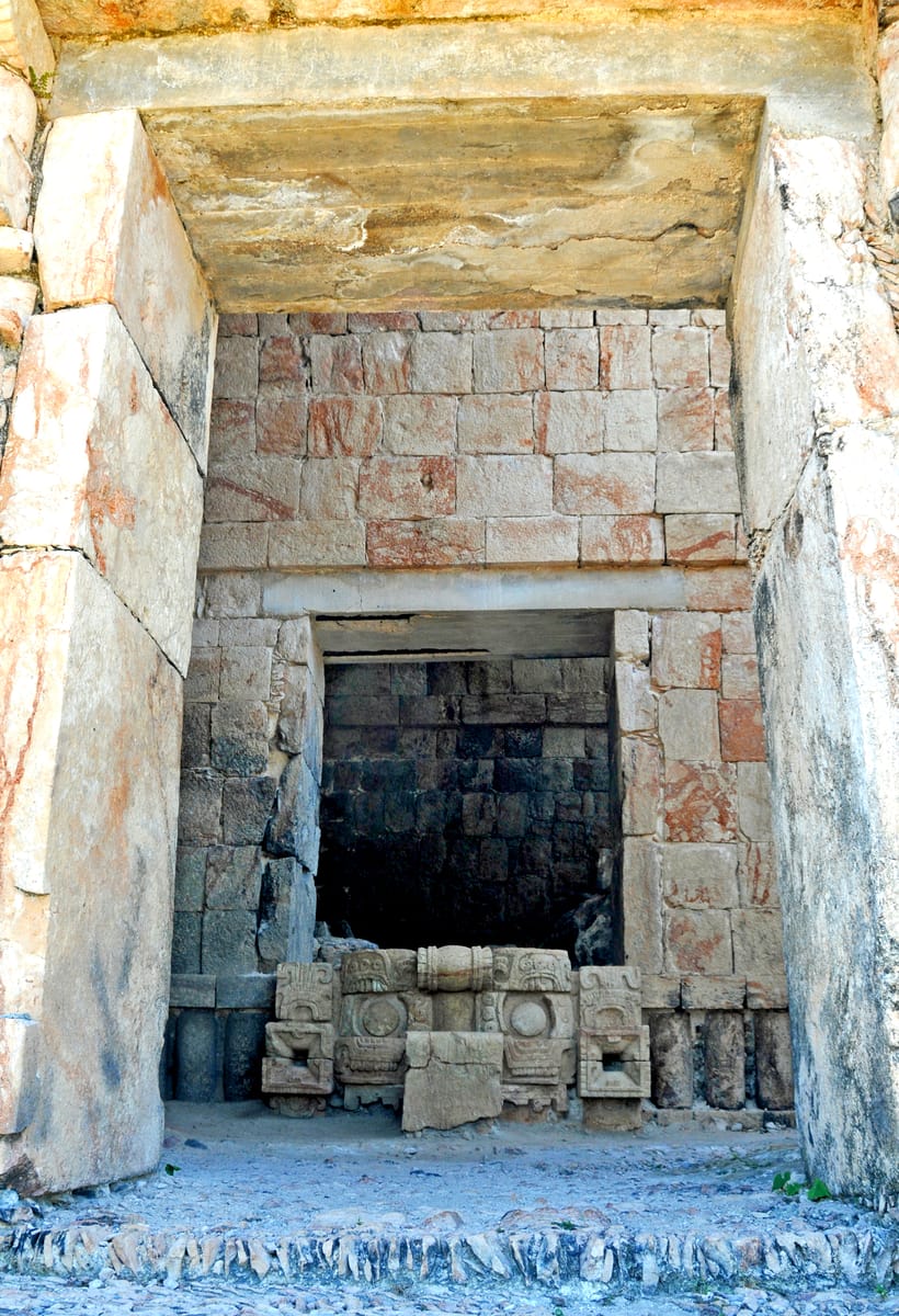 Inside the building, masks are turned into architecture: their thick stone snouts are laid as the treads of a stairway up to the rear rooms.