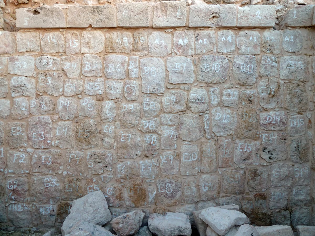 Restoration in progress at Kabah: fallen veneer stones chalked with grid codes so each block can be returned to its original position in the wall.