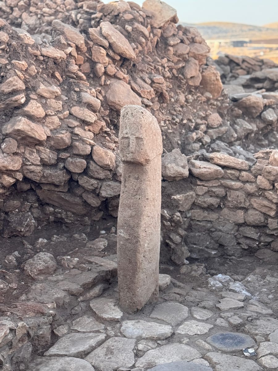 A T-shaped pillar carved with a human face, standing against an excavated wall at Karahan Tepe.