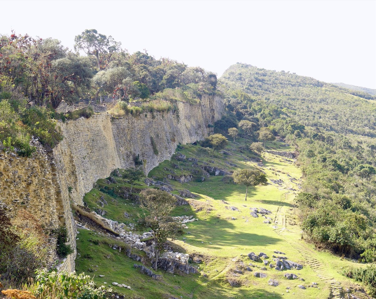 The perimeter wall running along the crest of the ridge, showing the scale of the platform the Chachapoya raised roughly 3,000 metres above the valley.