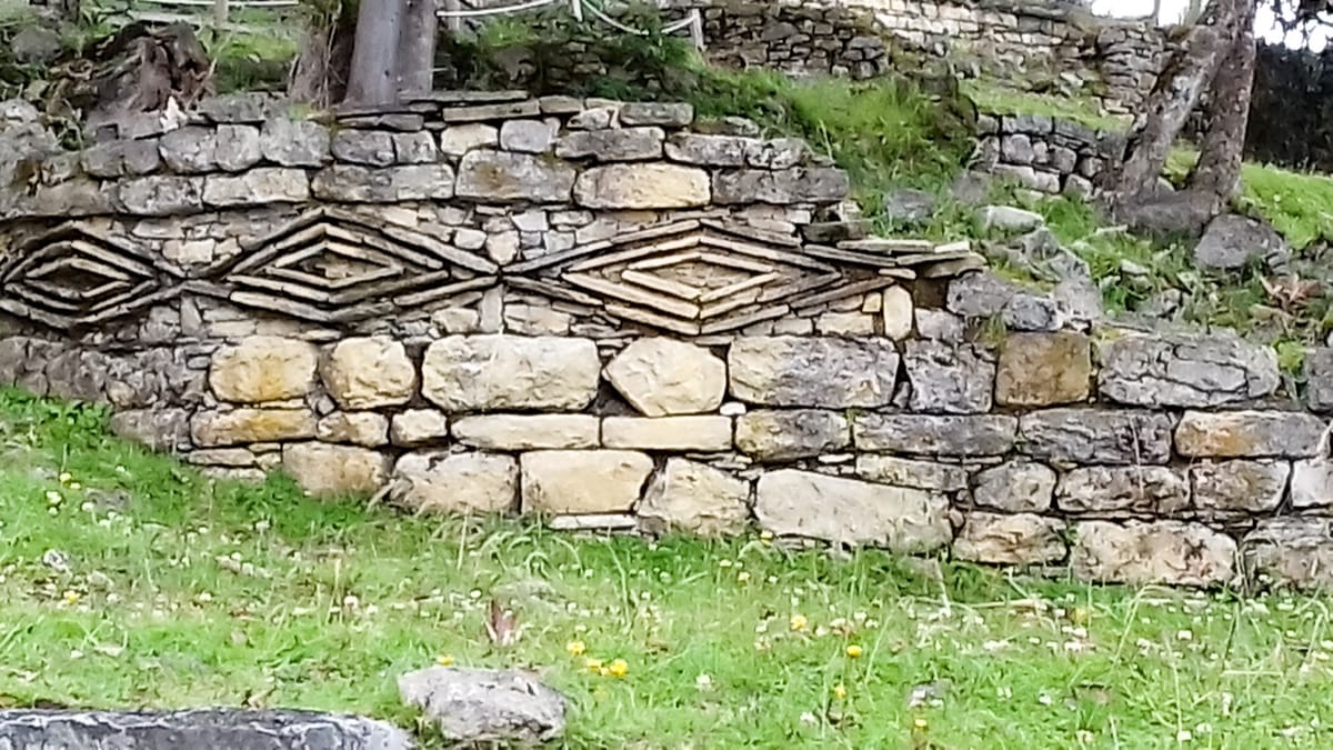 A wall decorated with the rhomboid and zigzag friezes characteristic of Chachapoya architecture, set into the coursed limestone of a circular building.