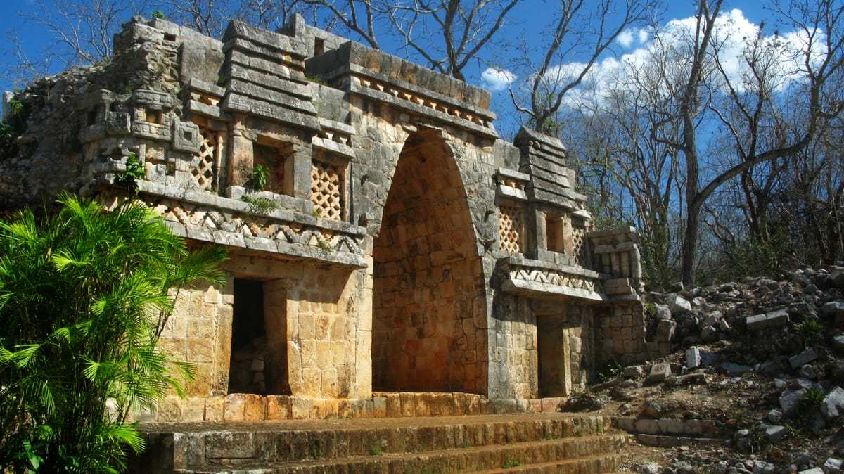 The northwest face, with latticework panels, two niches that still hold traces of stuccowork, and miniature stone models of thatched Maya houses above them. The smooth, almost pointed soffit of the passage is a corbelled vault dressed to look like a curve.