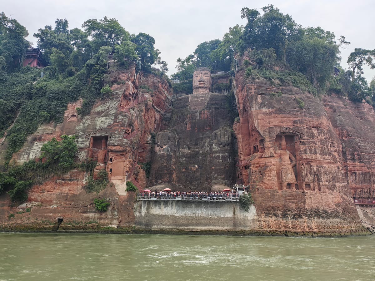 A frontal view of the colossal figure, carved in a serene, upright seated posture directly out of the cliff face.