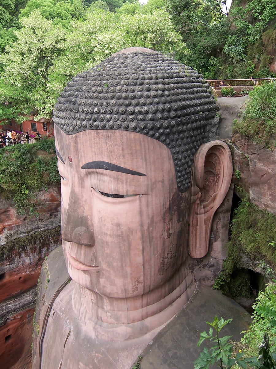 Visitors on the cliffside stairway beside the Buddha give a sense of the statue's immense scale.