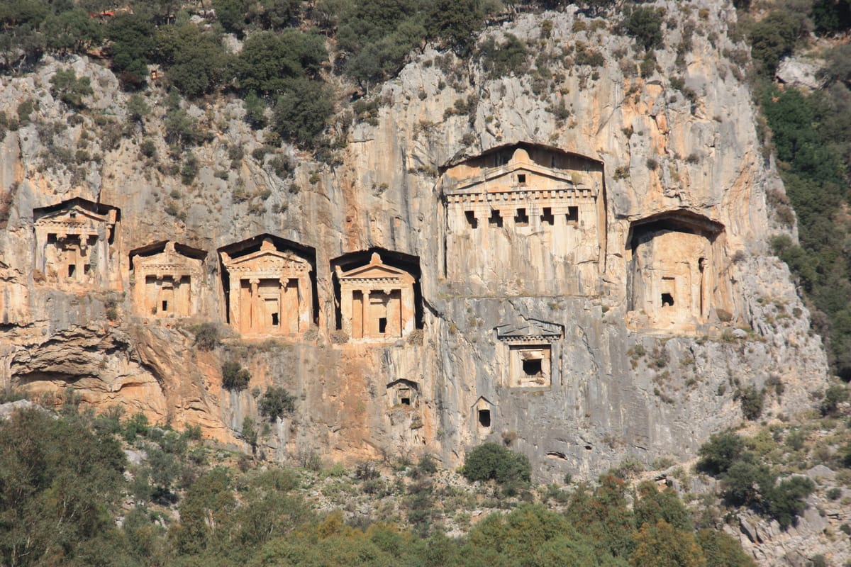 Temple-type tombs in the cliff at Kaunos, above Dalyan. Kaunos was a Carian city, not a Lycian one, but its masons adopted the same rock-cut form; the large tomb at upper right was left unfinished.