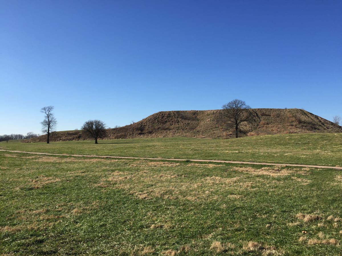 Approaching Monks Mound from ground level, with the modern staircase climbing toward its terraces.