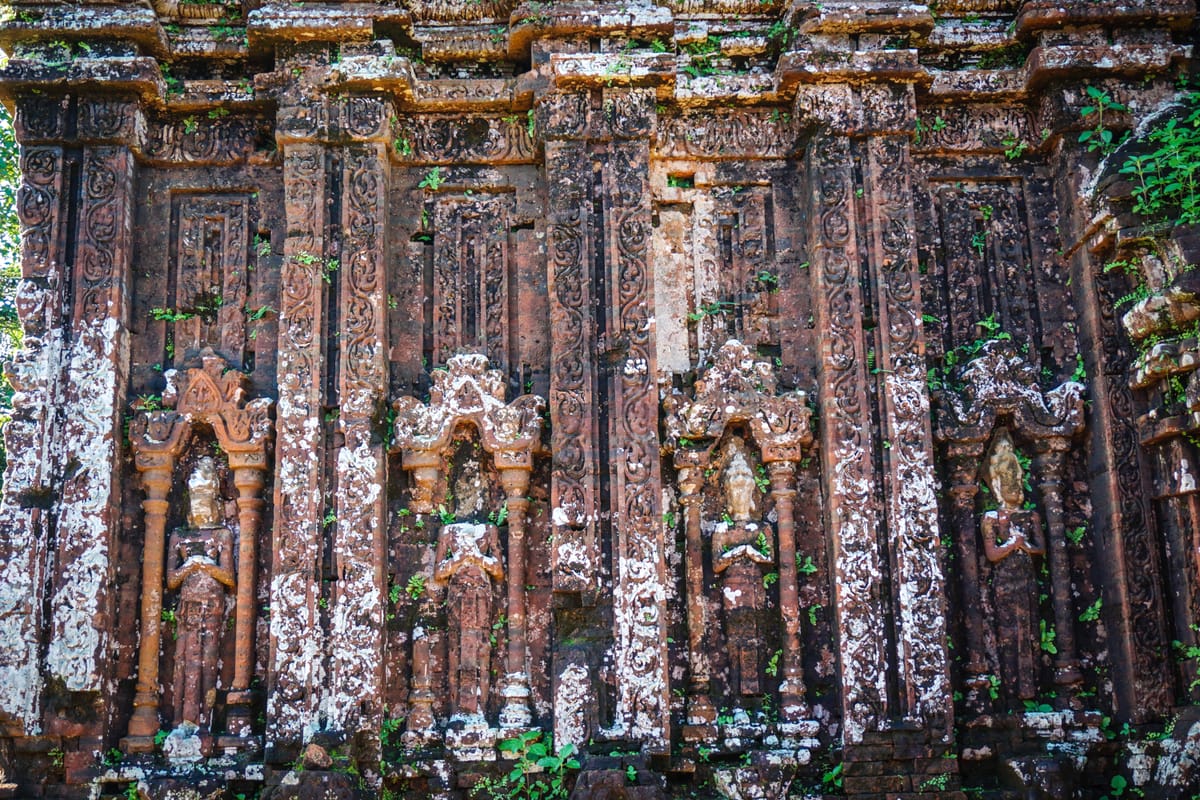 Decorative pilasters, foliate scrollwork, and niche figures carved directly into the assembled brick face of a Mỹ Sơn tower — ornament cut into the built wall rather than into individual bricks beforehand.