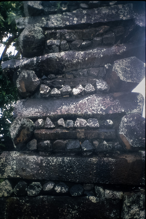 Detail of a wall built from stacked columnar basalt pieces, laid in crisscross header-and-stretcher courses without mortar.