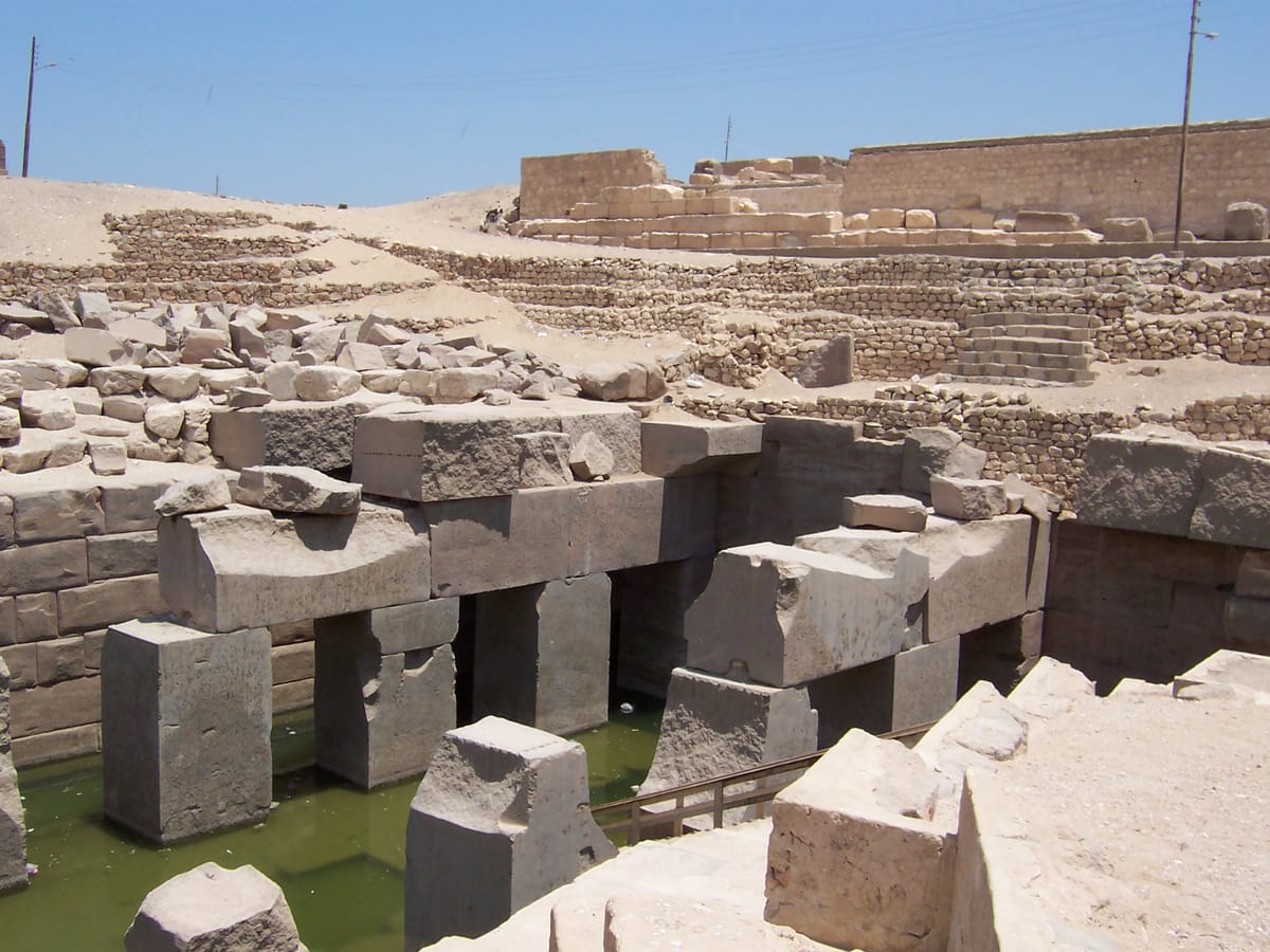A closer view of the plain, monolithic granite pillars and the recessed cells, with algae-greened water pooling in the channel — the deliberately unadorned, massive masonry that gives the Osirion its archaic character.