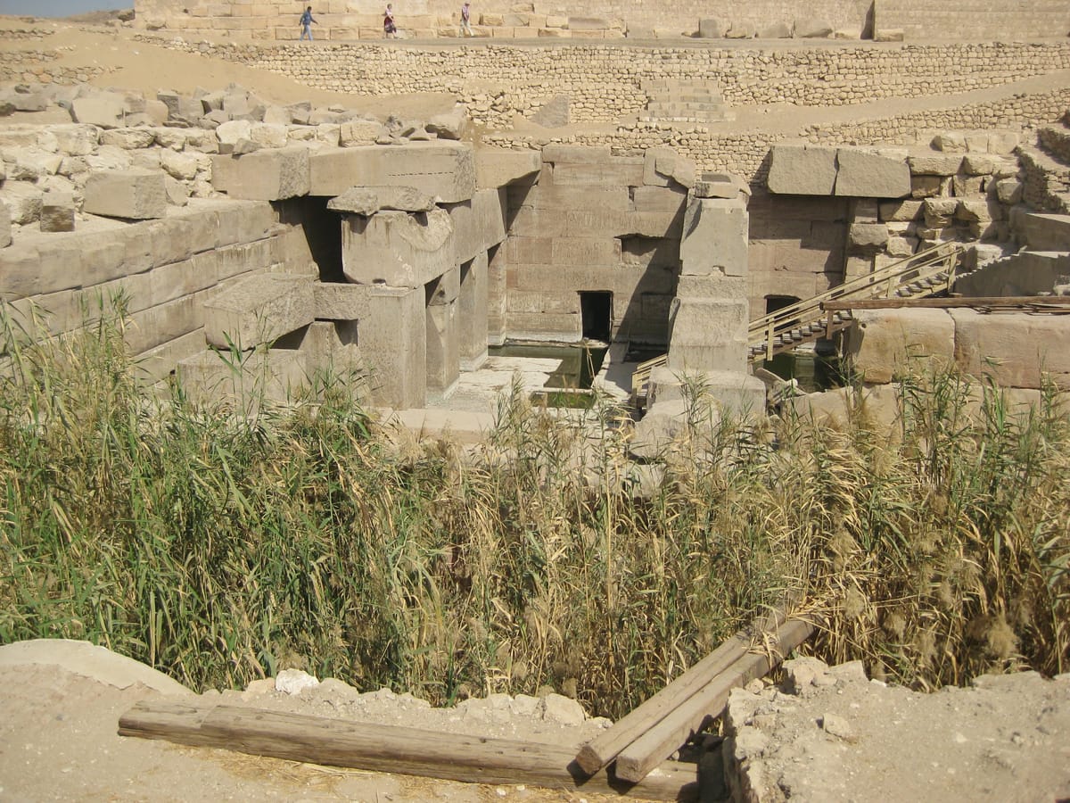 The Osirion in its landscape: the megalithic hall sits in a deep pit cut well below the surrounding desert and the mud-brick ruins of Abydos, a reminder that the whole structure was built downward to reach groundwater.
