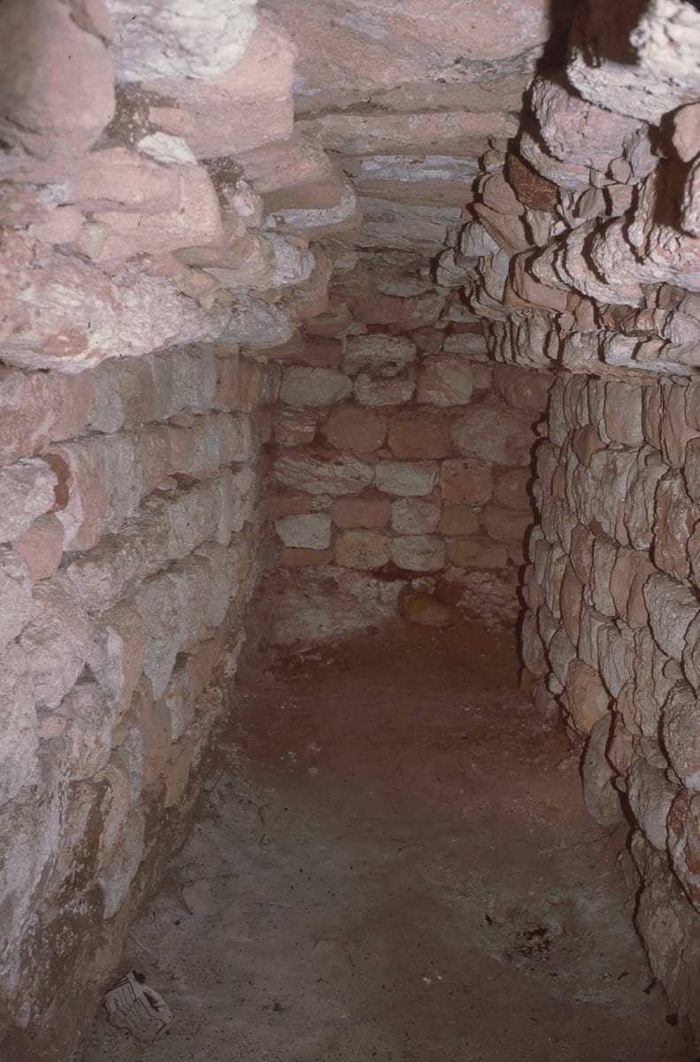 Inside the Satunsat: a corbel-vaulted interior gallery, its stone courses stepping inward until they nearly meet overhead. The passages are narrow, low, and completely dark.