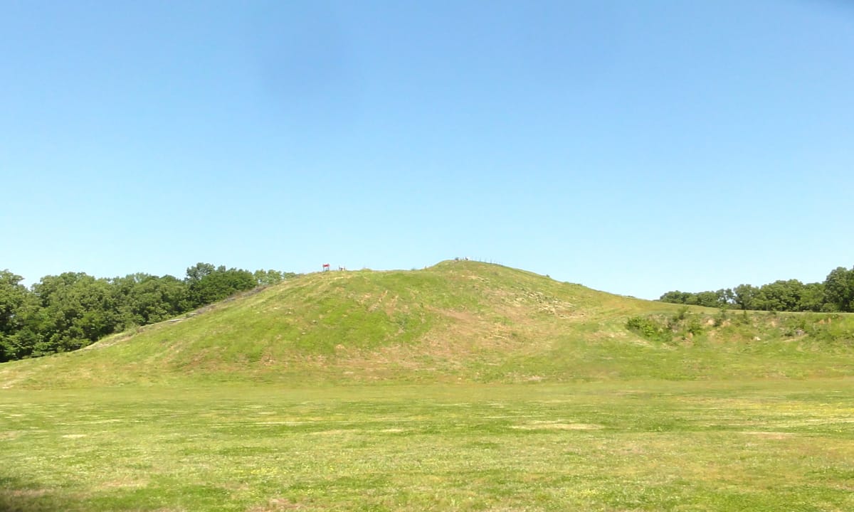 A ground-level view of one of the Poverty Point mounds, its grassy slope rising from the flat plaza — the scale that had to be built up one basket-load at a time.