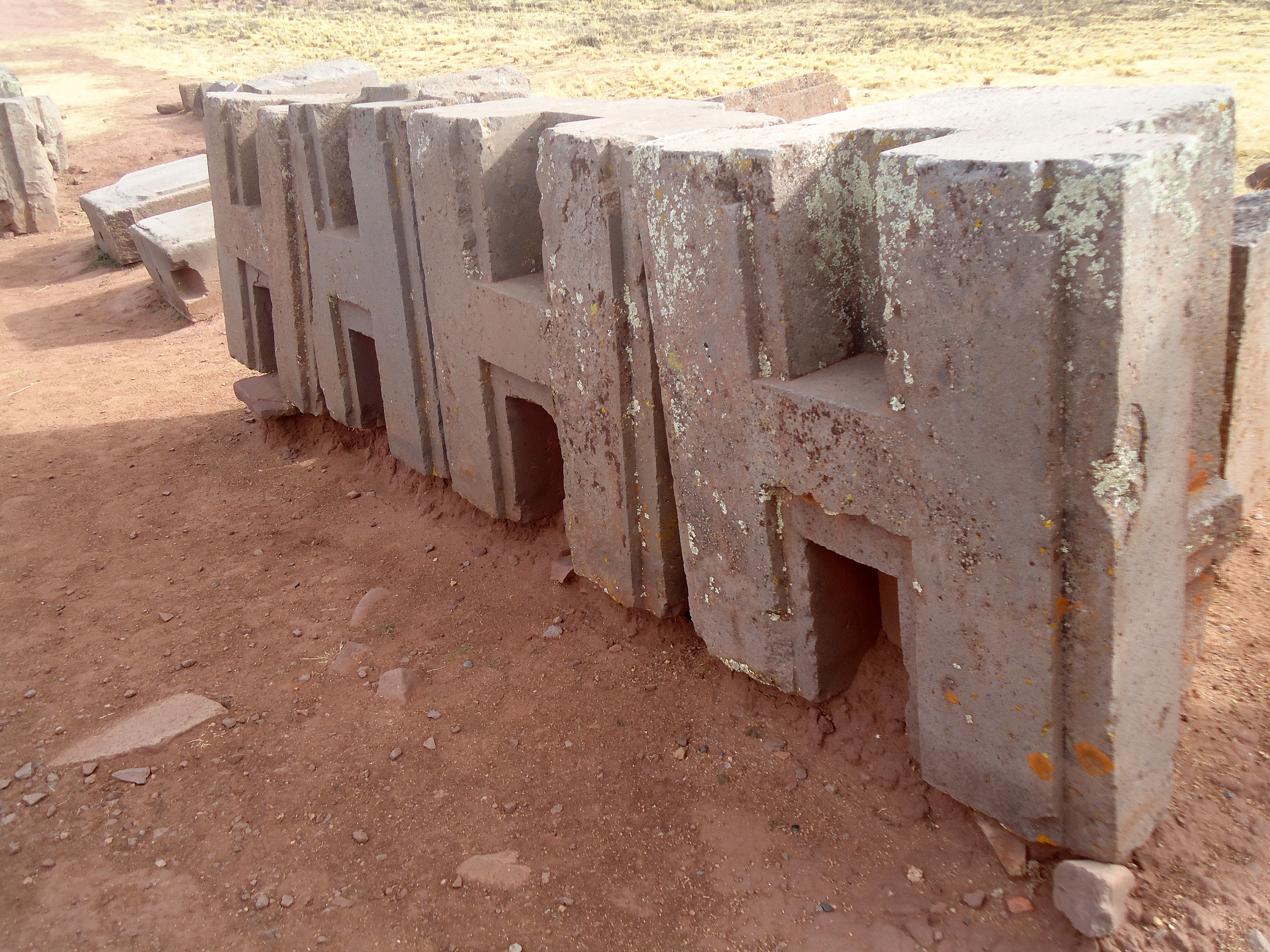 A wall of Puma Punku's characteristic 'H'-profile andesite blocks, cut to a repeating modular shape.