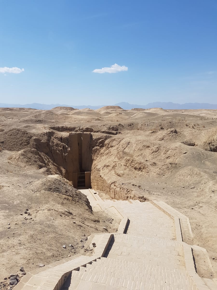 The main access cut into the Qasabeh qanat, set in the ring-mound landscape left by 427 shafts — each low crater is the spoil hauled up from one vertical well.