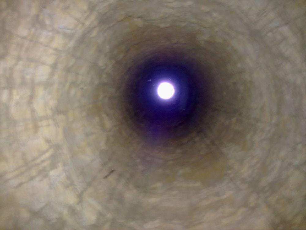 Looking up a shaft of the Gonabad qanat from inside the tunnel — the daylight disc that gave the diggers air, a spoil route, and their only fixed reference point underground.