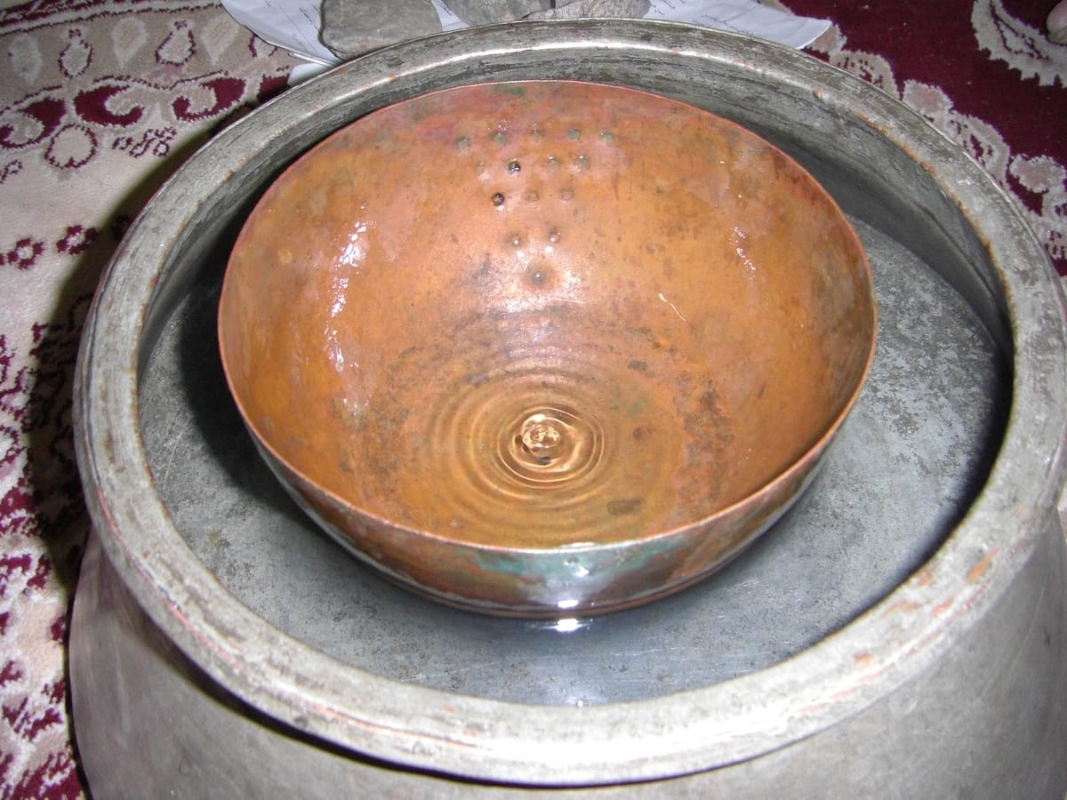 A fenjaan, the Persian sinking-bowl water clock: a pierced copper bowl floated in a larger vessel until it filled and sank, timing each shareholder's turn at the qanat water.