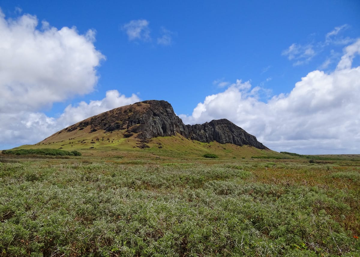 Rano Raraku seen from the south — the tuff crater whose cliff face was the island's single statue quarry, with moai visible scattered across the lower slope.