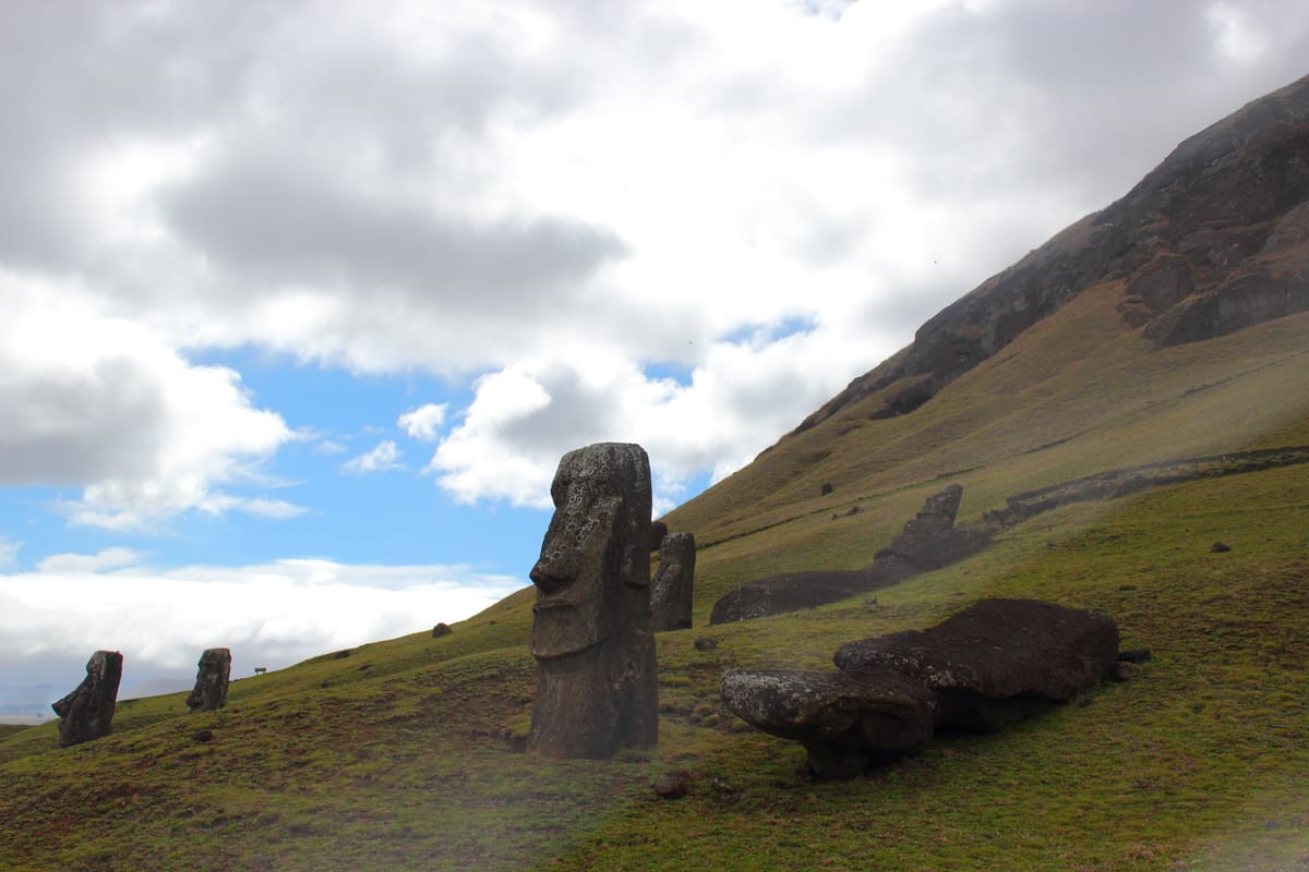 An upright moai buried to its chest beside another left lying flat on the slope, below the quarry cliff.