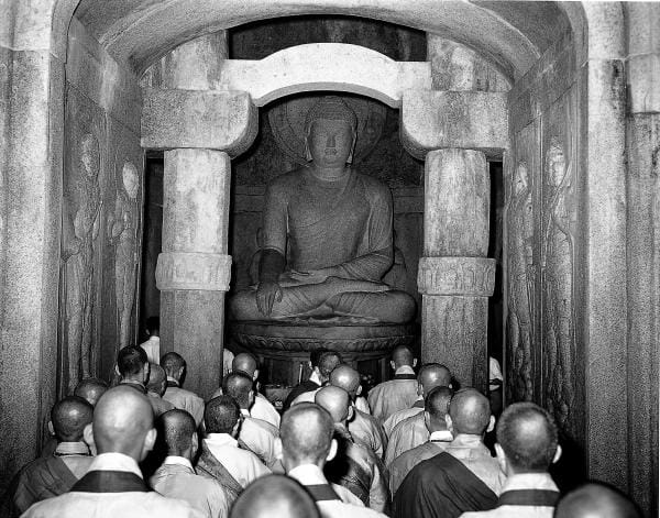 Monks assembled before the Buddha at the ceremony marking the completion of the restoration, 2 July 1964 — the project that sealed the grotto behind a second concrete dome and mechanical climate control.