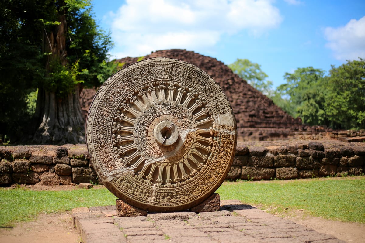 A carved Dvaravati-style stone Dharmachakra (Wheel of the Law) with the stupa of Khao Klang Nai in the background, inside the inner walled city.