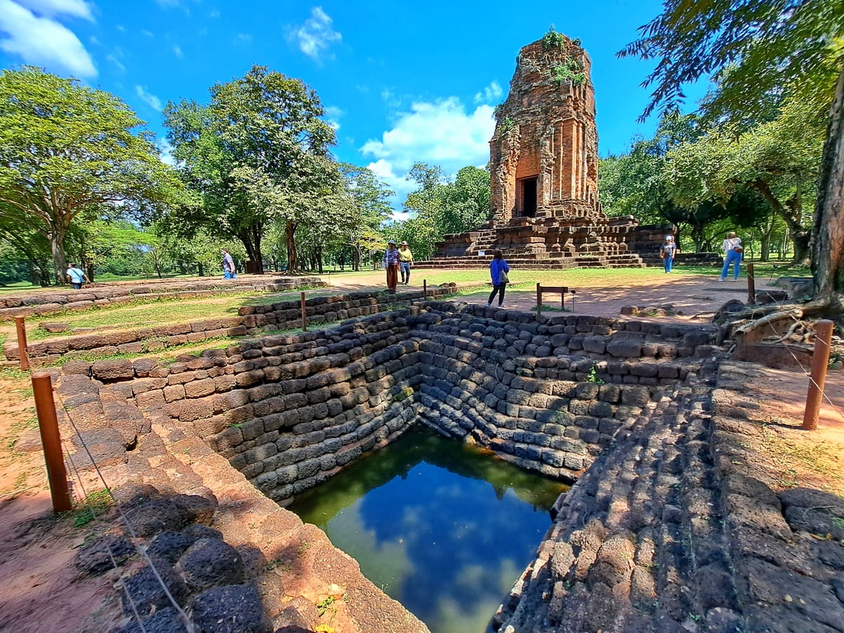 The ruins of Prang Si Thep, an 11th-12th century Khmer-style laterite tower originally built as a Hindu Shaivite shrine, beside an ancient stone-lined pond.