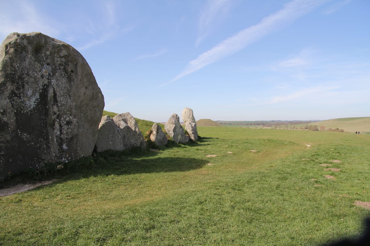 West Kennet Long Barrow in the foreground with Silbury Hill visible in the distance, illustrating the density of Neolithic monuments in the Avebury landscape.