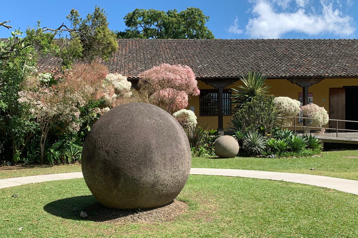 A large stone sphere on the grounds of the Museo Nacional de Costa Rica, with a smaller sphere visible behind it, illustrating the range of sizes produced.