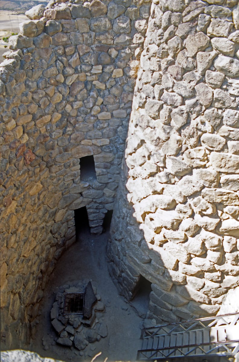Looking down into the fortified core: the massive dry-stone walls of the central keep and a corner tower flanking the inner courtyard, with the well below.