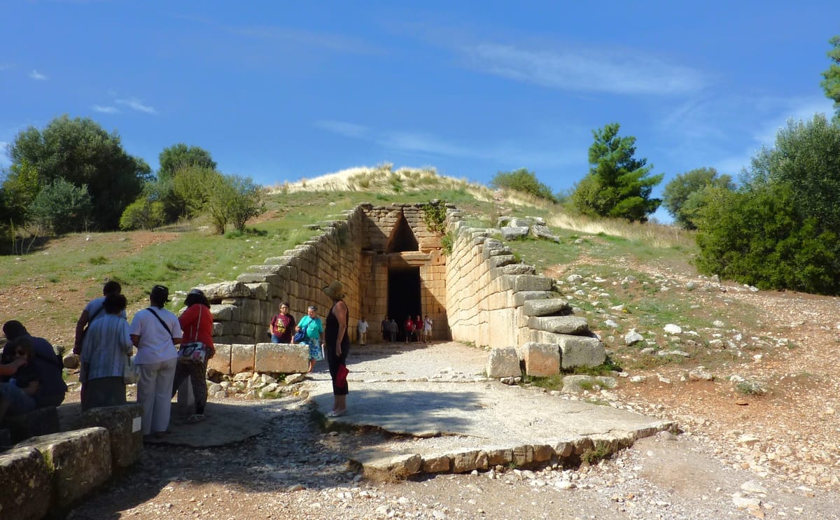 The tomb from outside, with visitors for scale: the whole beehive chamber sits inside the hillside under an earthen mound, entered along a 36-metre cut approach.